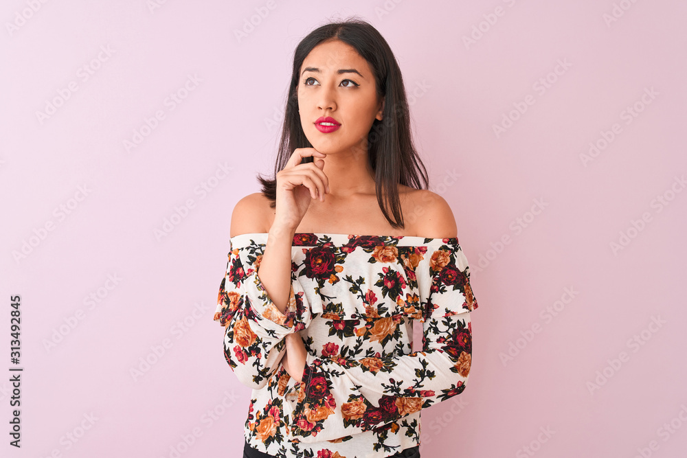 Young chinese woman wearing floral t-shirt standing over isolated pink background with hand on chin thinking about question, pensive expression. Smiling with thoughtful face. Doubt concept. Young chinese woman wearing floral t-shirt standing over isolated pink background with hand on chin thinking about question, pensive expression. Smiling with thoughtful face. Doubt concept.