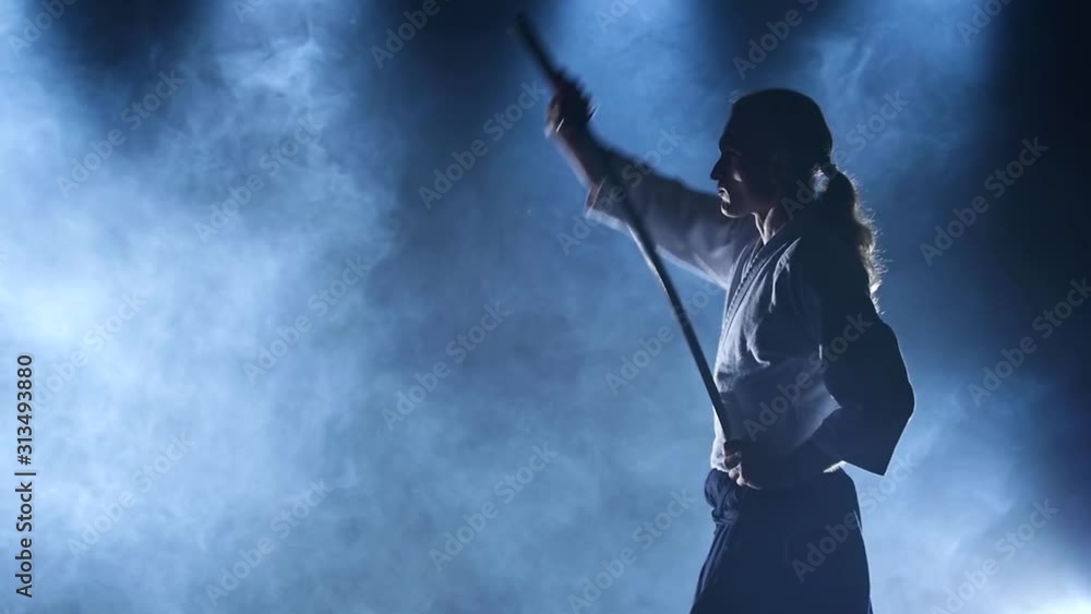 Man fighting at Aikido training with japanese sword katana in martial arts school. Healthy lifestyle and sports concept in dark studio with smoke and lighting. Slow motion. Close up. Man fighting at Aikido training with japanese sword katana in martial arts school. Healthy lifestyle and sports concept in dark studio with smoke and lighting. Slow motion. Close up.