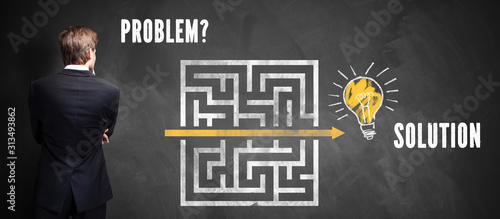 businessman thinking about how to solve a problem in front of blackboard with a drawn maze