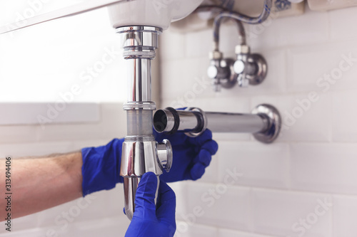Obraz na płótnie Plumber repairs and maintains chrome siphon under the washbasin. Plumber at work in bathroom, plumbing assemble and install concept w salonie