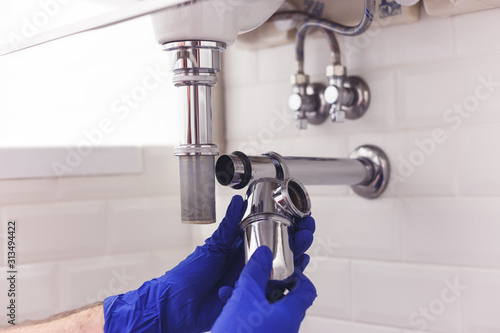 Plumber repairs and maintains chrome siphon under the washbasin Fototapeta