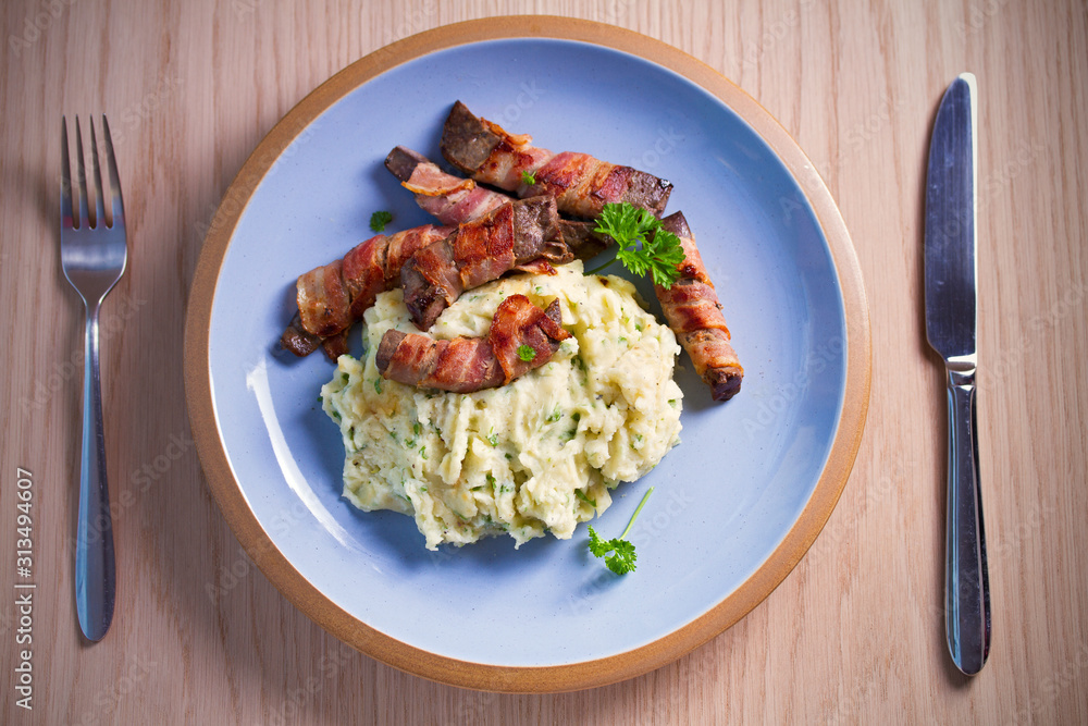 Beef liver wrapped in bacon with mash potato on blue table. Overhead horizontal image Beef liver wrapped in bacon with mash potato on blue table. Overhead horizontal image