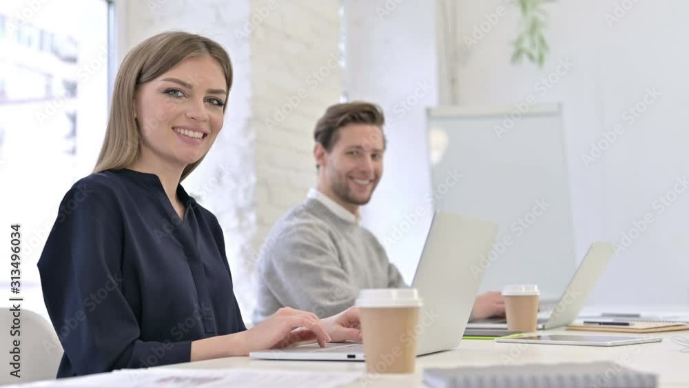 Attractive Creative Team working on Laptop and Smiling at the Camera Attractive Creative Team working on Laptop and Smiling at the Camera