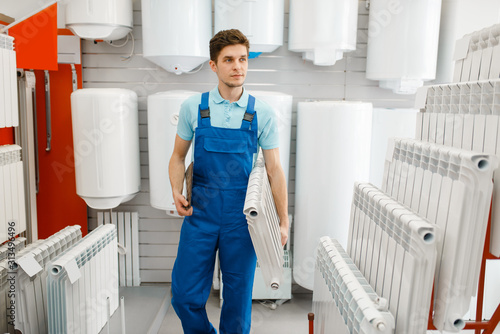 Fotografie Plumber holds heating radiator, plumbering store