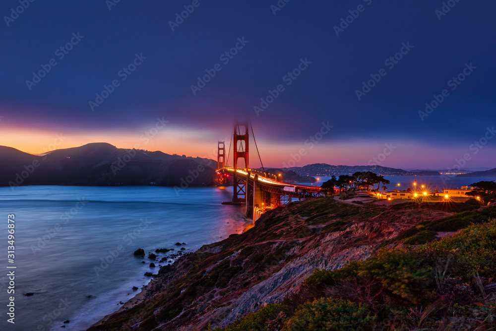 The fog lifts above the Golden Gate Bridge after the sun has set along the San Francisco shoreline