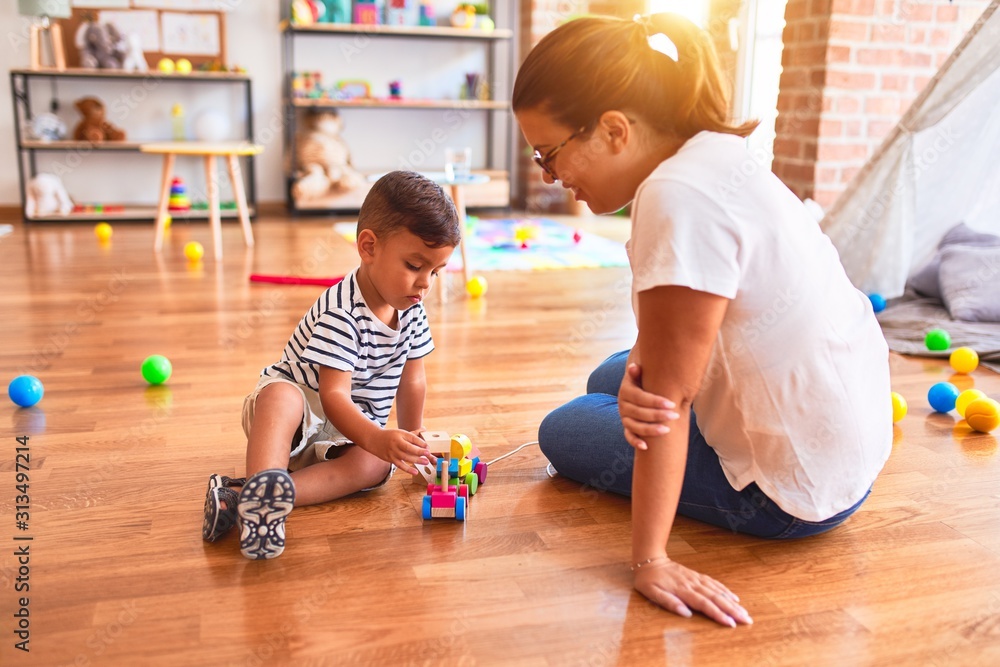 Fototapeta premium Beautiful teacher and toddler boy playing with train at kindergarten