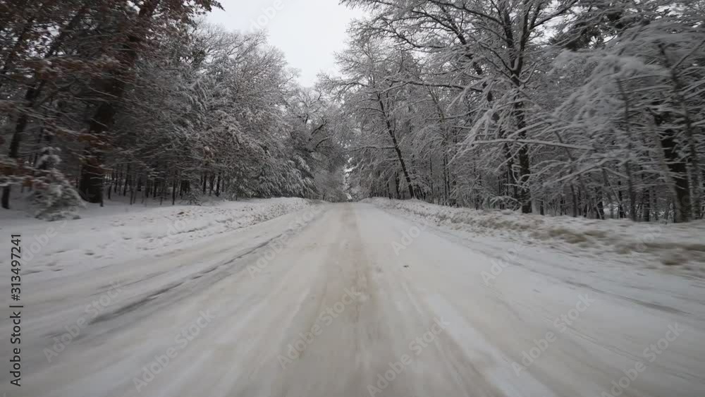 Driving a car on asphalt road covered with snow and ice. Road surrounded by trees with fresh snow. Front car view Driving a car on asphalt road covered with snow and ice. Road surrounded by trees with fresh snow. Front car view