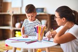 Beautiful teacher and toddler boy drawing draw using colored pencils at kindergarten