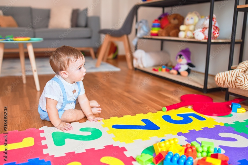 Fototapeta premium Beautiful toddler sitting on puzzle carpet playing with building blocks at kindergarten