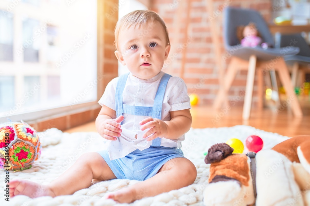 Beautiful toddler sitting on the blanket around lots of toys at kindergarten Beautiful toddler sitting on the blanket around lots of toys at kindergarten