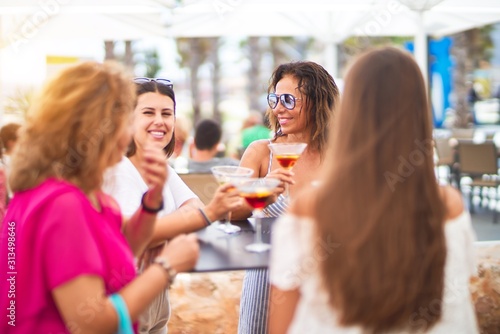 Beautiful group of women sitting at terrace of restaurant drinking cocktails speaking and smiling