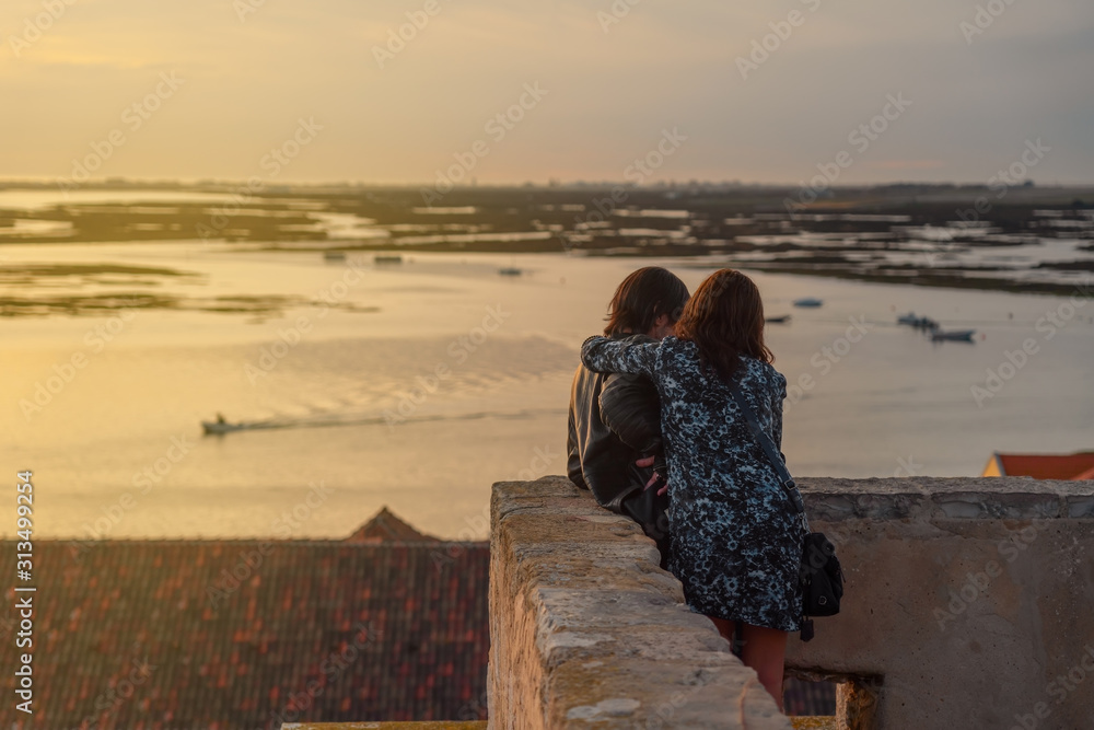 A couple on the castle wall are enjoying over the sea sunset.