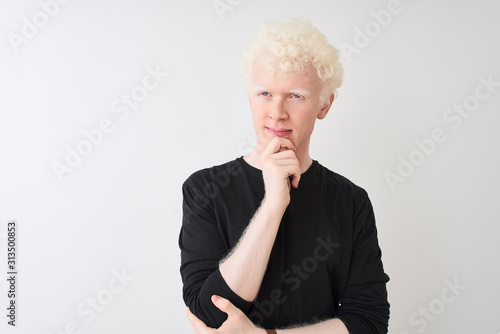 Young albino blond man wearing black t-shirt standing over isolated white background with hand on chin thinking about question, pensive expression. Smiling with thoughtful face. Doubt concept.