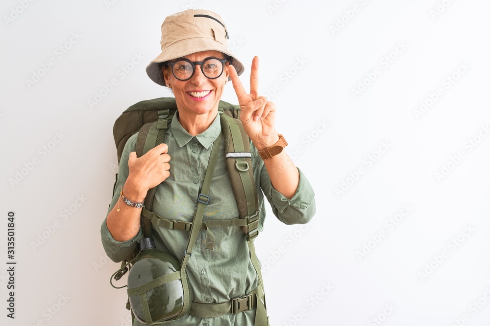 Middle age hiker woman wearing backpack canteen hat glasses over isolated white background showing and pointing up with fingers number two while smiling confident and happy. Middle age hiker woman wearing backpack canteen hat glasses over isolated white background showing and pointing up with fingers number two while smiling confident and happy.