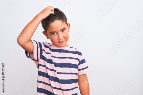 Beautiful kid boy wearing casual striped t-shirt standing over isolated white background confuse and wonder about question. Uncertain with doubt, thinking with hand on head. Pensive concept.