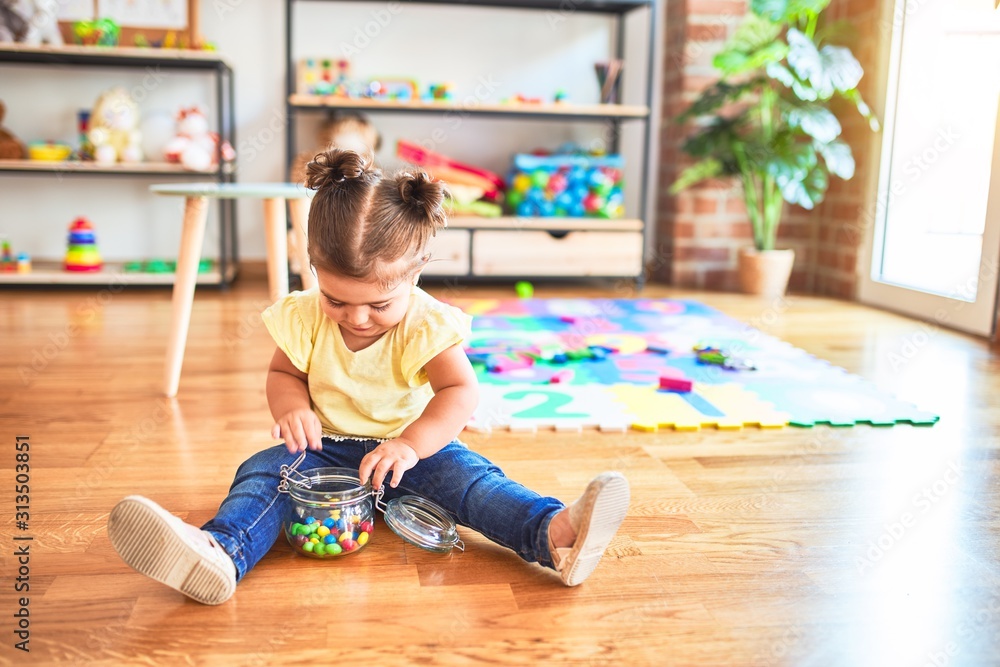 Beautiful toddler sitting on the floor with jar of chocolate colored balls at kindergarten Beautiful toddler sitting on the floor with jar of chocolate colored balls at kindergarten