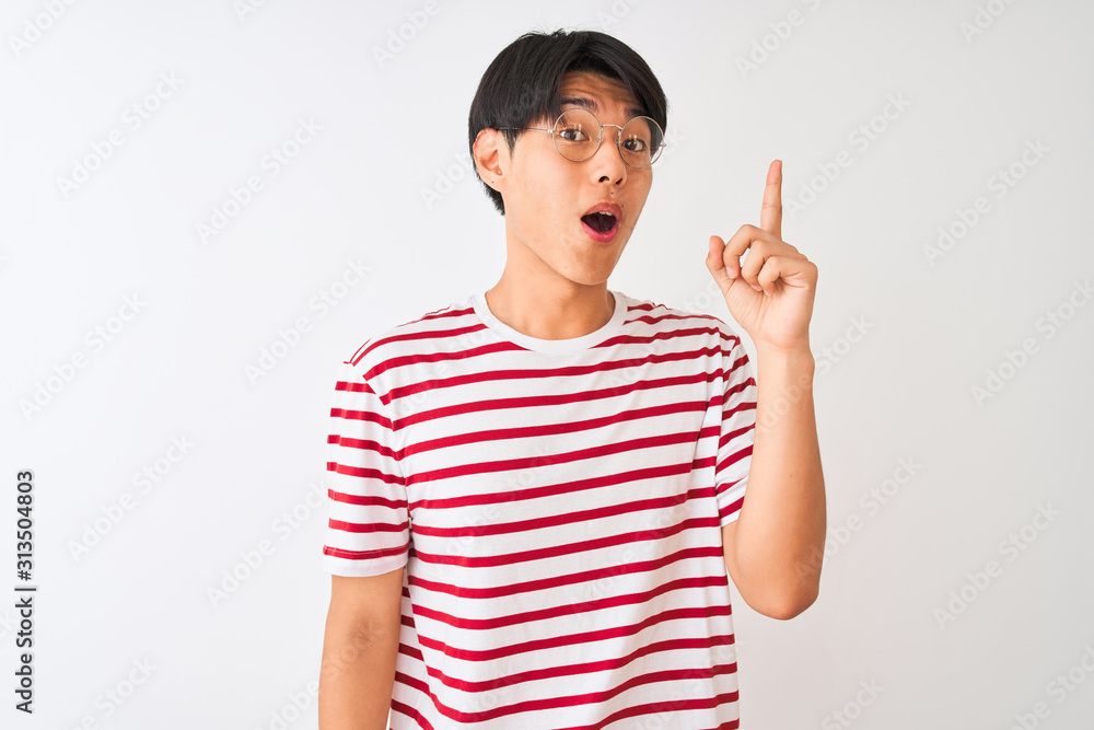 Young chinese man wearing glasses and striped t-shirt standing over isolated white background pointing finger up with successful idea. Exited and happy. Number one. Young chinese man wearing glasses and striped t-shirt standing over isolated white background pointing finger up with successful idea. Exited and happy. Number one.