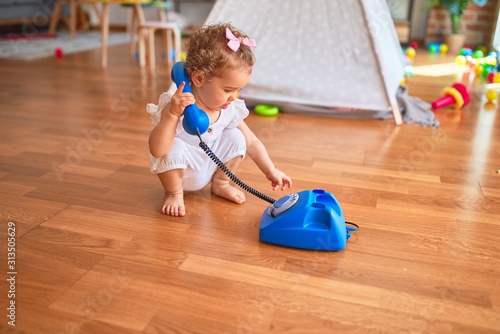 Beautiful caucasian infant playing with toys at colorful playroom. Happy and playful calling with vitange telephone at kindergarten.