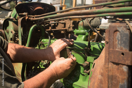Close up of agricultural mechanic working on an antique green farm tractor outside in the sunshine