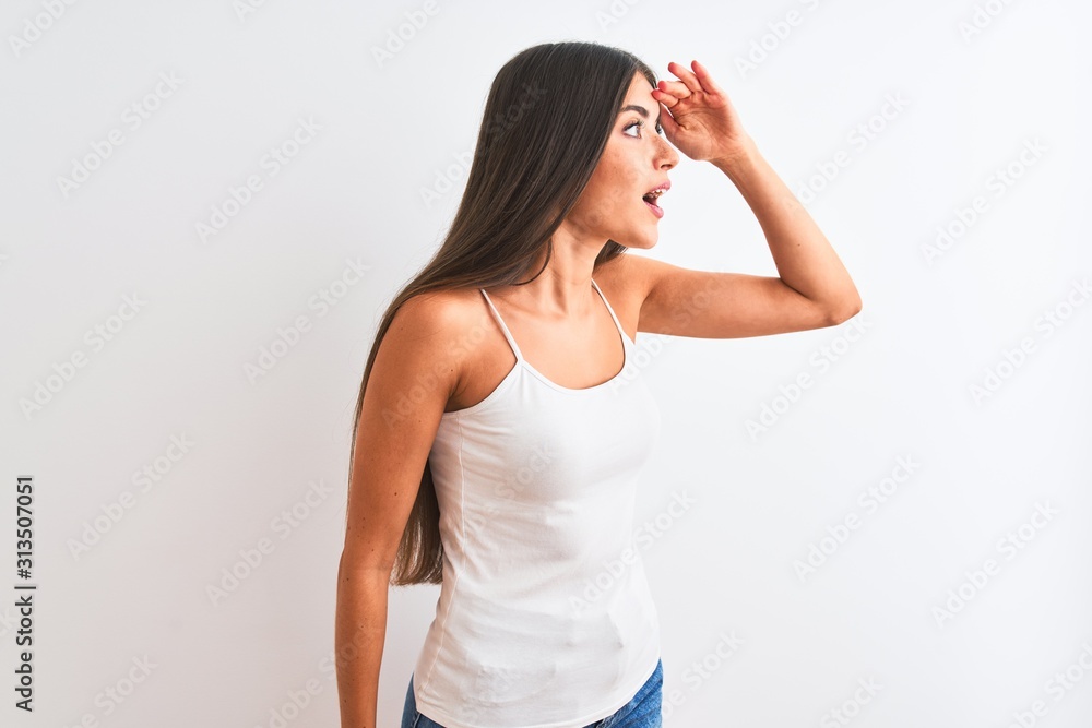 Young beautiful woman wearing casual t-shirt standing over isolated white background very happy and smiling looking far away with hand over head. Searching concept. Young beautiful woman wearing casual t-shirt standing over isolated white background very happy and smiling looking far away with hand over head. Searching concept.