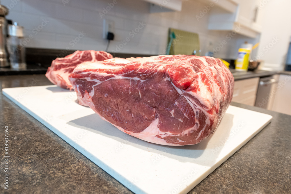 Two prime rib beef roasts sitting on a white plastic cutting board in a restaurant kitchen. The meat has marble and bones in them. The cutting board is large and lays on a counter top.
