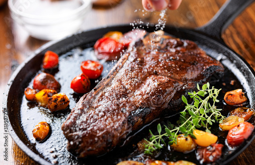 sprinking sea salt on a ny strip steak cooked in a iron skilelt photo