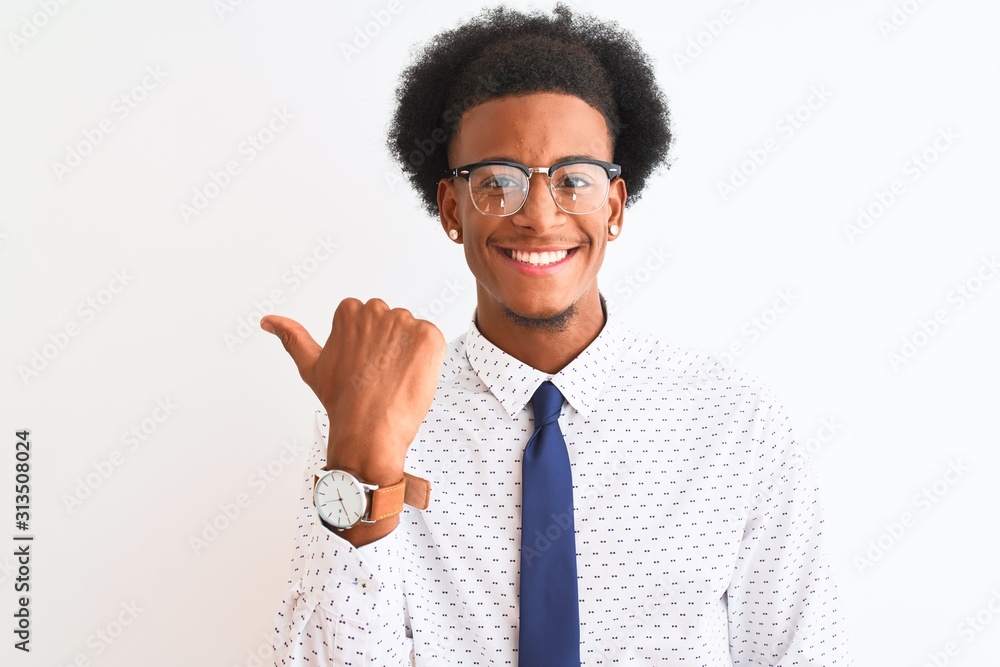 Young african american businessman wearing tie and glasses over isolated white background smiling with happy face looking and pointing to the side with thumb up. Young african american businessman wearing tie and glasses over isolated white background smiling with happy face looking and pointing to the side with thumb up.