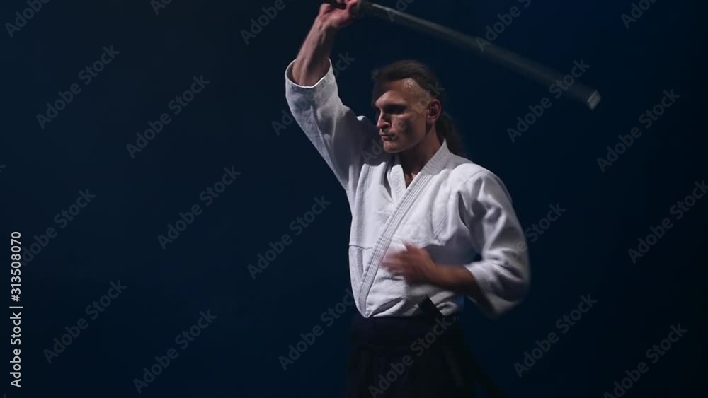 Man fighting at Aikido training with japanese sword katana in martial arts school. Healthy lifestyle and sports concept in the dark studio. Slow motion. Close up. Man fighting at Aikido training with japanese sword katana in martial arts school. Healthy lifestyle and sports concept in the dark studio. Slow motion. Close up.