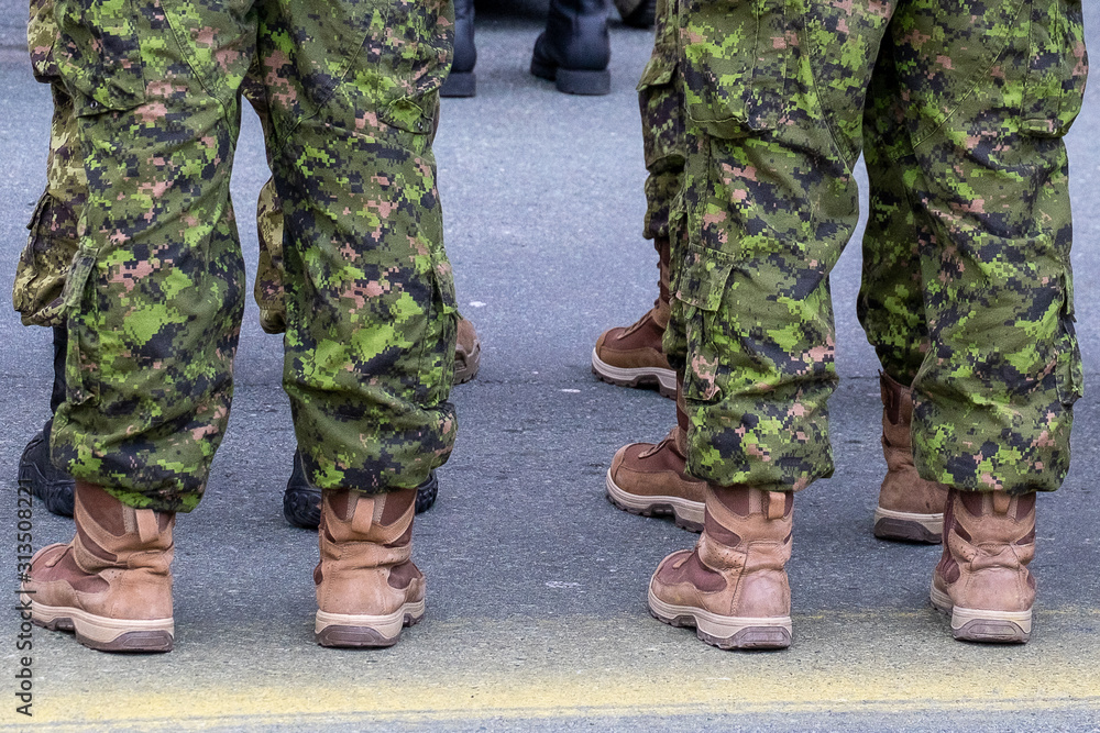 Multiple soldiers stand in camouflage fatigues and tan-colored desert boots. The men are lined up in two rows. The green uniforms are tucked inside high top boots. Multiple soldiers stand in camouflage fatigues and tan-colored desert boots. The men are lined up in two rows. The green uniforms are tucked inside high top boots.