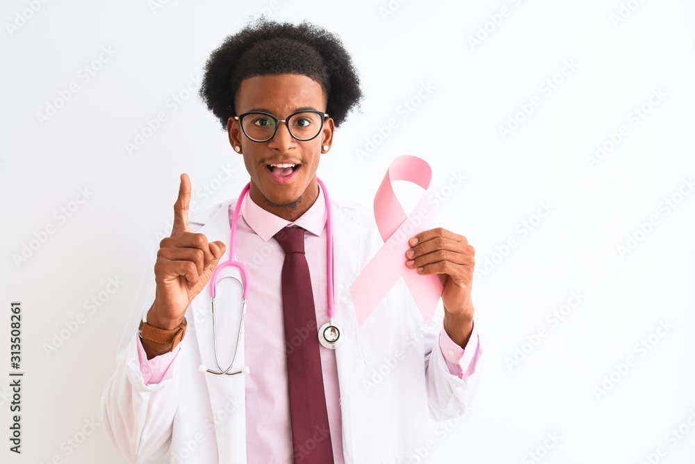 Young african american doctor man holding cancer ribbon over isolated white background surprised with an idea or question pointing finger with happy face, number one Young african american doctor man holding cancer ribbon over isolated white background surprised with an idea or question pointing finger with happy face, number one