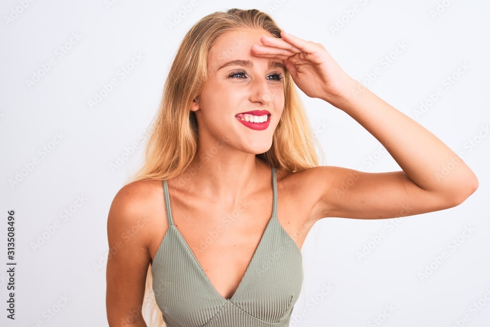 Young beautiful woman wearing casual green t-shirt standing over isolated white background very happy and smiling looking far away with hand over head. Searching concept. Young beautiful woman wearing casual green t-shirt standing over isolated white background very happy and smiling looking far away with hand over head. Searching concept.