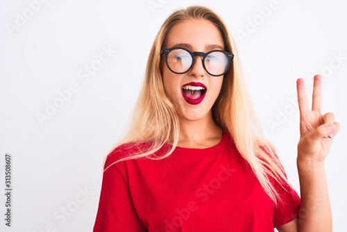 Young beautiful woman wearing red t-shirt and glasses standing over isolated white background smiling with happy face winking at the camera doing victory sign. Number two.