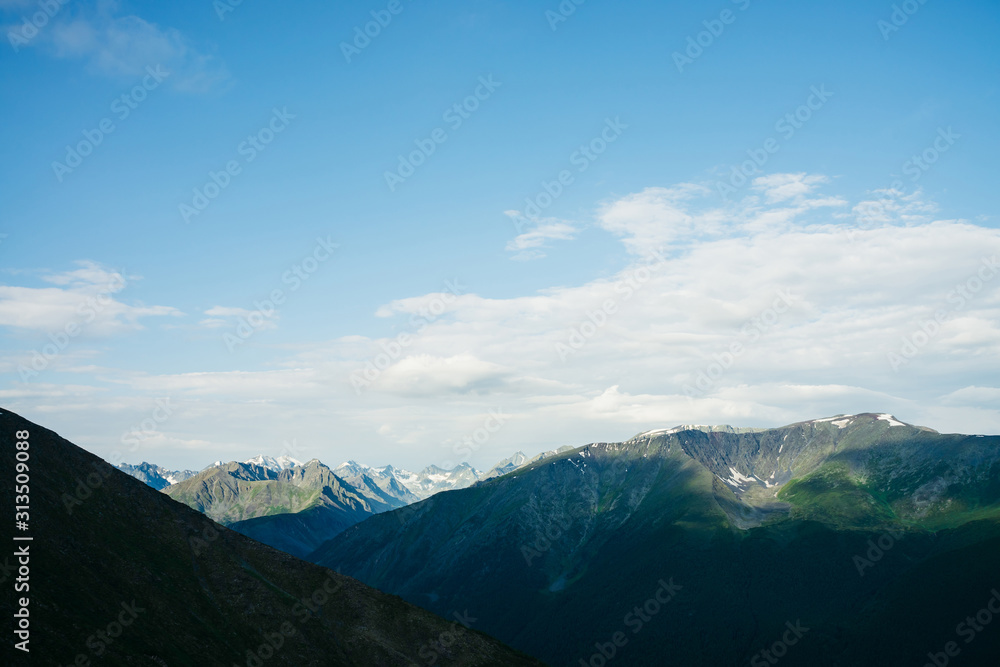 Atmospheric alpine landscape to giant mountain range. Snow on high rocky ridges. Forest on massive slopes. Tranquil atmosphere. Shadows of clouds on big mountains. Majestic scenery on high altitude.