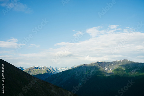 Atmospheric alpine landscape to giant mountain range. Snow on high rocky ridges. Forest on massive slopes. Tranquil atmosphere. Shadows of clouds on big mountains. Majestic scenery on high altitude. © Daniil