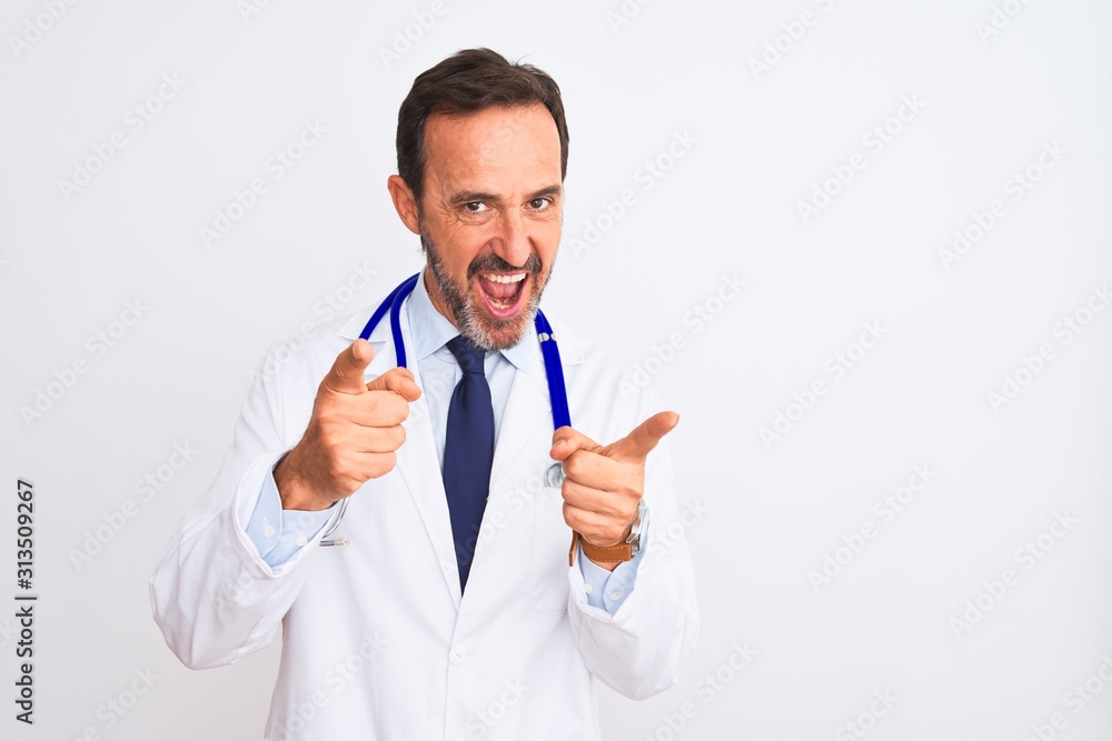 Middle age doctor man wearing coat and stethoscope standing over isolated white background pointing fingers to camera with happy and funny face. Good energy and vibes.
