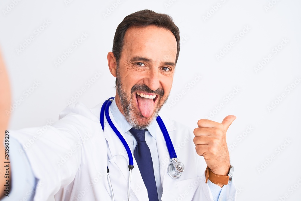 Middle age doctor man wearing stethoscope make selfie over isolated white background pointing and showing with thumb up to the side with happy face smiling Middle age doctor man wearing stethoscope make selfie over isolated white background pointing and showing with thumb up to the side with happy face smiling
