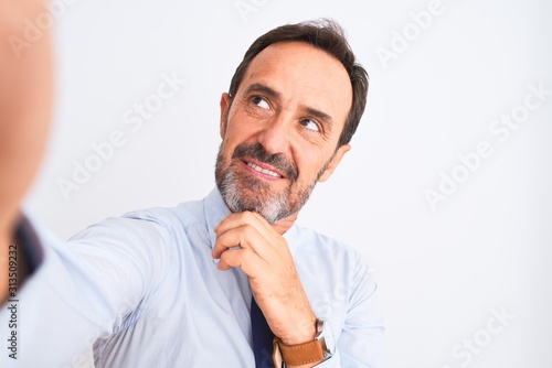 Middle age businessman wearing tie make selfie standing over isolated white background serious face thinking about question, very confused idea