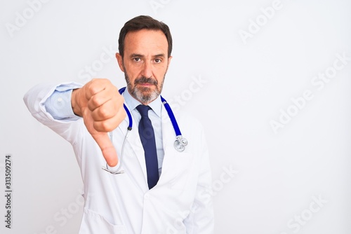 Middle age doctor man wearing coat and stethoscope standing over isolated white background looking unhappy and angry showing rejection and negative with thumbs down gesture. Bad expression.