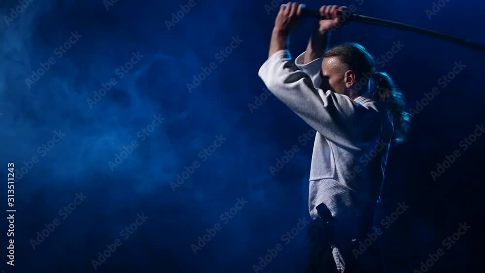 Man fighting at Aikido training with japanese sword katana in martial arts school. Healthy lifestyle and sports concept in the dark studio. Slow motion. Close up. Man fighting at Aikido training with japanese sword katana in martial arts school. Healthy lifestyle and sports concept in the dark studio. Slow motion. Close up.