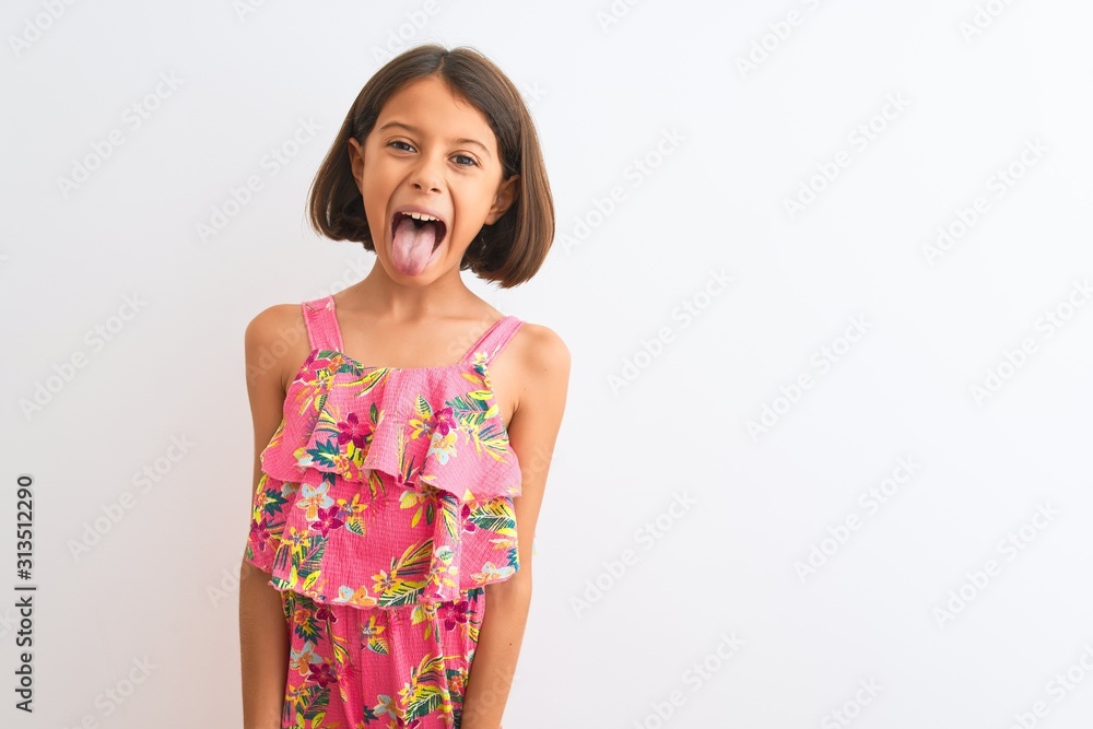 Young beautiful child girl wearing pink floral dress standing over isolated white background sticking tongue out happy with funny expression. Emotion concept. Young beautiful child girl wearing pink floral dress standing over isolated white background sticking tongue out happy with funny expression. Emotion concept.