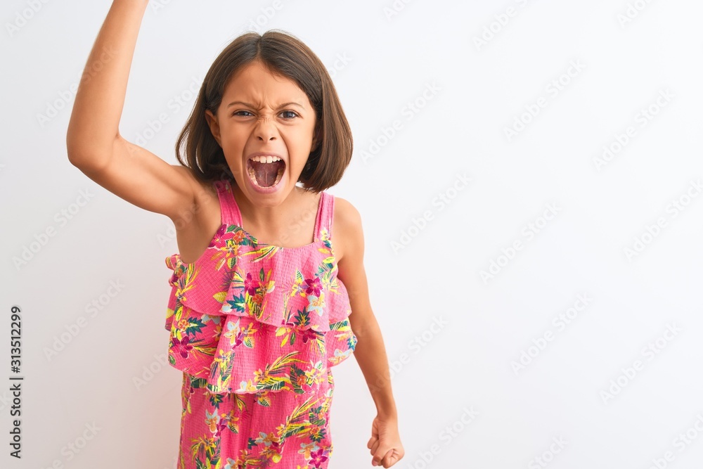 Young beautiful child girl wearing pink floral dress standing over isolated white background angry and mad raising fist frustrated and furious while shouting with anger. Rage and aggressive concept. Young beautiful child girl wearing pink floral dress standing over isolated white background angry and mad raising fist frustrated and furious while shouting with anger. Rage and aggressive concept.