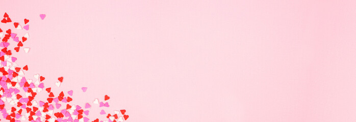 Valentines Day corner border banner with candy heart sprinkles over a pink textured background. Copy space.