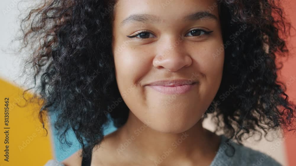 Slow motion portrait of pretty Afro-American student looking at camera smiling standing alone on colorful background. Individuality, people and happiness concept. Slow motion portrait of pretty Afro-American student looking at camera smiling standing alone on colorful background. Individuality, people and happiness concept.
