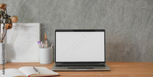 Cropped shot of trendy workplace with mock-up laptop computer and office supplies on wooden table and grey wall © bongkarn