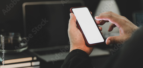 Close-up view of businessman using smartphone while working on his project in dark luxury workplace