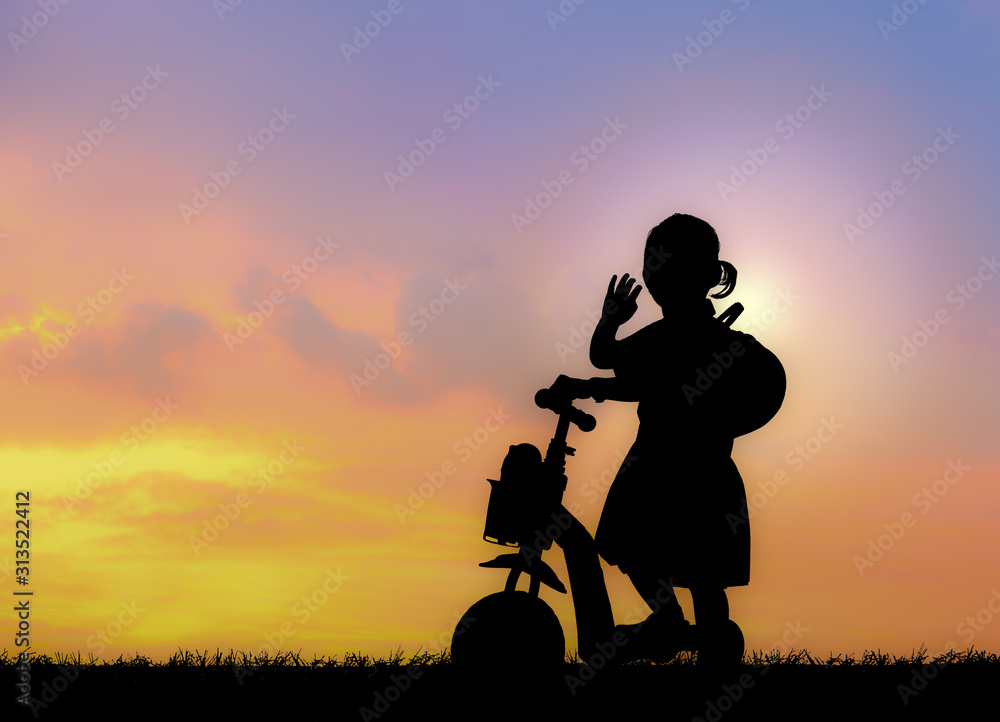 Silhouette of little girl using a scooter in nature sunset