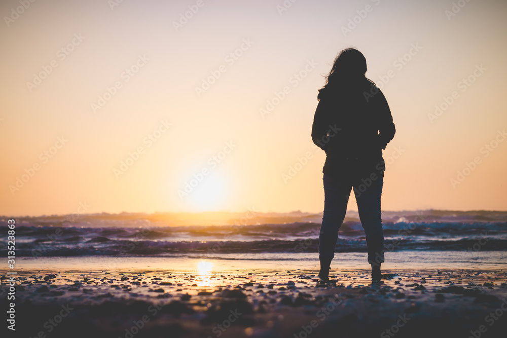 Silhouette of woman with coat on the beach with sunset background