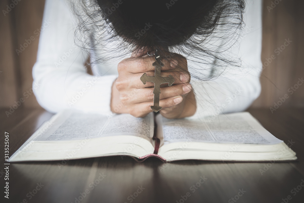 Naklejka premium The girl wishes to God. In the hand there was a cross and placed on the Bible. Concept of prayer, prayer for salvation from suffering, Christ's religion. Catholicism, God, Heaven, God.