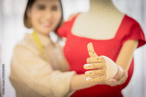 Hand thumb up of mannequin with red clothes and blur Asian designer woman background, Start up. Business ideas concepts.