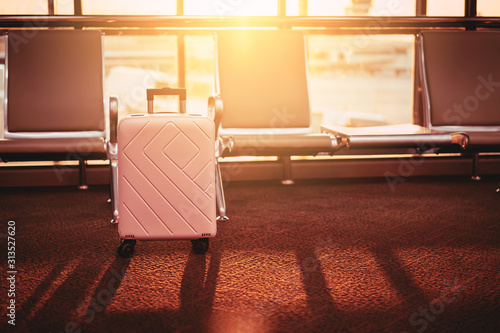 Travel bag and chair in airport terminal gate with window sunset light background. Travel adventure and vacation freedom concept.